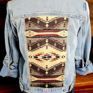 May include: Light blue denim jacket with a colorful geometric patterned fabric panel on the back. The panel features brown, red, and cream colors. The sleeves are rolled up, revealing a patterned lining.
