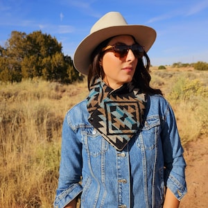 May include: A woman wearing a denim jacket and a patterned neck warmer. She is wearing a wide-brimmed hat and sunglasses. The background is a field of tall grass.