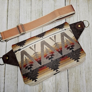 Puede incluir: Ri&ntilde;onera rectangular con un estampado geom&eacute;trico del suroeste en crema, marr&oacute;n, rojo y beige. Tiene un detalle de cuero marr&oacute;n, una cremallera plateada y una correa ajustable beige con un cierre met&aacute;lico. La bolsa est&aacute; dise&ntilde;ada para llevarse en la cintura o cruzada.