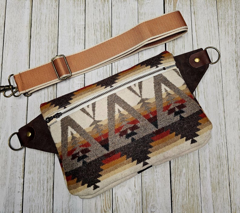 Puede incluir: Ri&ntilde;onera rectangular con un estampado geom&eacute;trico del suroeste en crema, marr&oacute;n, rojo y beige. Tiene un detalle de cuero marr&oacute;n, una cremallera plateada y una correa ajustable beige con un cierre met&aacute;lico. La bolsa est&aacute; dise&ntilde;ada para llevarse en la cintura o cruzada.