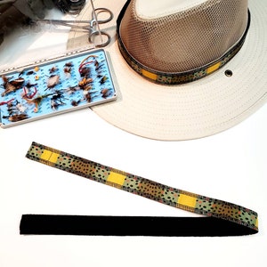 May include: A brown and yellow patterned fly fishing leader with a black elastic strap. The leader is made of braided material and has a speckled pattern.