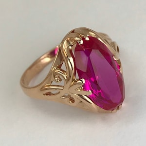 May include: A gold ring featuring a large, oval-shaped, pink gemstone set in a delicate, ornate design.