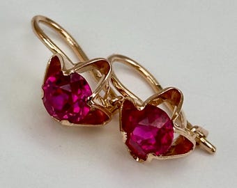 May include: A pair of gold earrings with red ruby stones. The earrings have a delicate floral design.