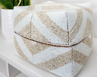 May include: A white and beige beaded storage basket with a geometric pattern. The basket is made of small beads woven together to create a textured surface.