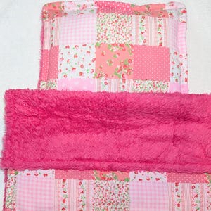 May include: A patchwork baby blanket and pillow set. The blanket features a mix of pink fabrics with floral, polka dot, and gingham patterns. A fluffy, hot pink, faux fur trim is sewn across the top. The pillow has a matching patchwork design.