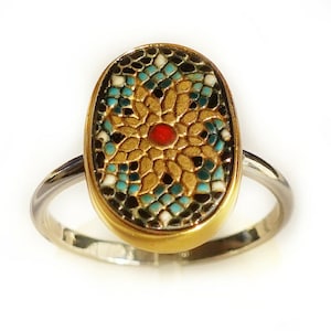 May include: A gold ring with a mosaic design featuring a red center and blue and black accents.