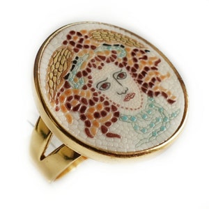May include: A gold ring with a white mosaic design featuring a woman's face. The mosaic is made of small, colorful tiles.