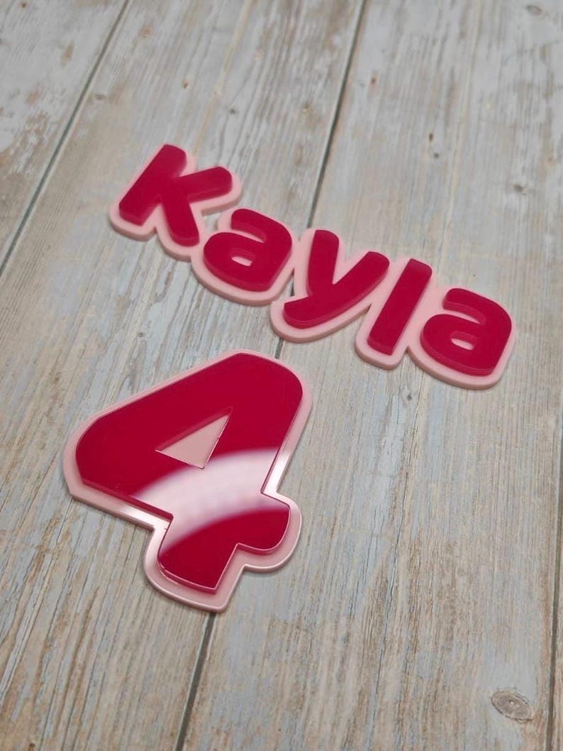 May include: A layered acrylic sign featuring the name Kayla in a bold, dark pink font with a light pink backing, accompanied by a separate layered acrylic number 4 in the same dark pink and light pink color scheme with a glossy finish.