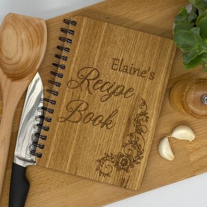 May include: A wooden recipe book with a spiral binding. The cover is engraved with the text "Elaine's Recipe Book" and a floral design.