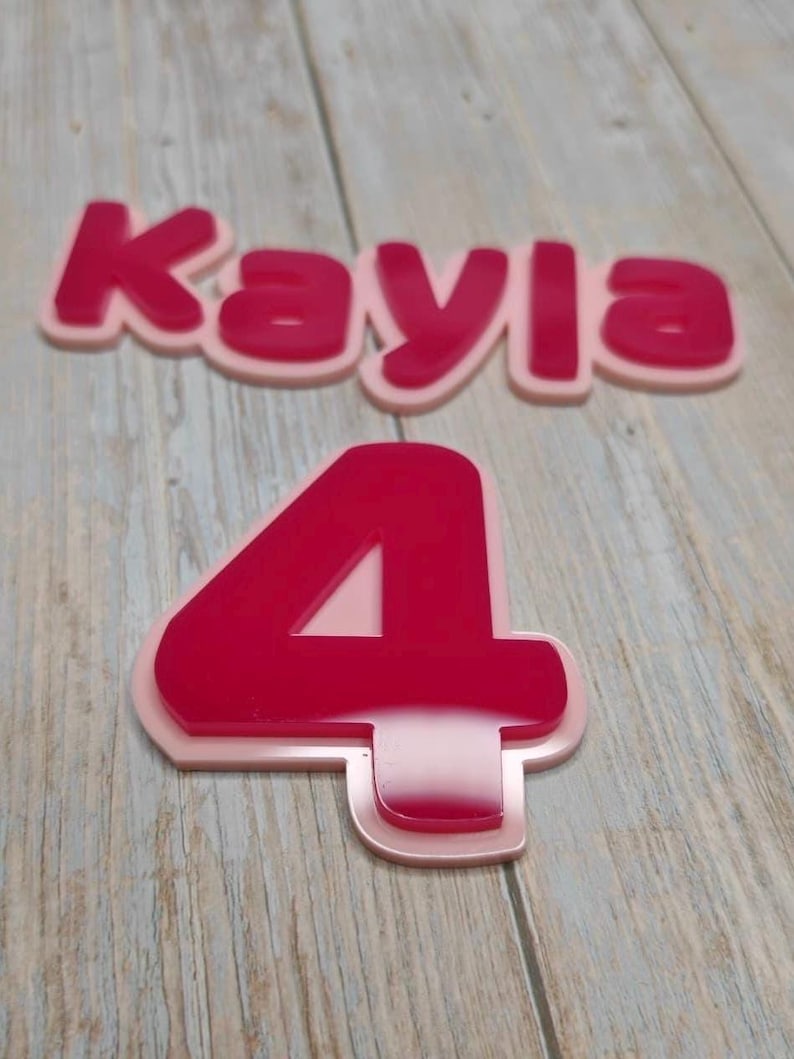 May include: A layered name sign reading Kayla in a bold, rounded font and a separate number four, both featuring a glossy dark pink top layer mounted onto a solid light pink base layer, creating a dimensional effect with clean, smooth edges.