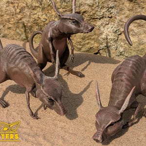 May include: Three brown, 3D printed, animal figurines with long snouts and ears. The figurines are posed in a variety of positions on a sandy surface.