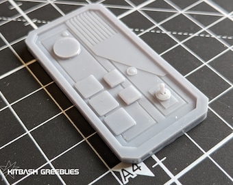 Könnte beinhalten: Ein graues Kunststoff-Bedienfeld mit einem runden Knopf, vier quadratischen Knöpfen und einem Joystick. Das Panel hat eine strukturierte Oberfläche und ist für den Einsatz in einem Modell oder einer Miniatur konzipiert.