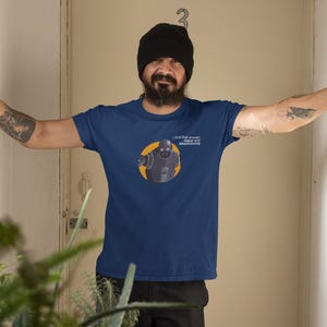 Puede incluir: Camiseta azul marino con un robot dentro de un círculo amarillo. El texto "I find that answer vague and unconvincing" está impreso encima del robot. La persona de la imagen lleva un gorro negro.