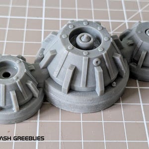 May include: Three grey plastic model pieces with a detailed, textured surface and a circular design. Each piece has a central hole and a raised ring around the edge.