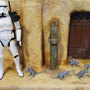 May include: A white stormtrooper action figure stands in front of a desert-themed backdrop.  Several small grey alien creatures are scattered on the ground in front of the figure.