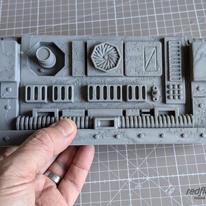 May include: Gray 3D printed model of a futuristic control panel with a textured surface, a circular vent, and a series of buttons and switches.
