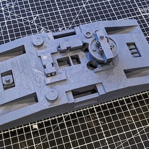 Peut inclure: Modèle 3D imprimé en plastique gris d'un vaisseau spatial ou d'un véhicule futuriste. Le modèle présente un design détaillé avec une tourelle circulaire sur le dessus et une série d'ouvertures rectangulaires sur les côtés.