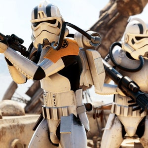 Puede incluir: Dos figuras de acción de stormtrooper blancas con cascos blanco y negro y armadura negra y naranja. Las figuras sostienen blásters y están de pie sobre una superficie arenosa.