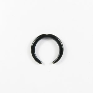 Peut inclure: Une bague ouverte noire en matériau lisse et poli. La bague est en forme de croissant de lune.