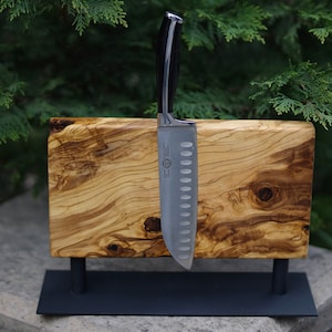 Könnte beinhalten: Ein magnetischer Messerhalter aus Olivenholz mit einem schwarzen Metallständer. Ein silbernes Messer mit schwarzem Griff ist am Halter befestigt.