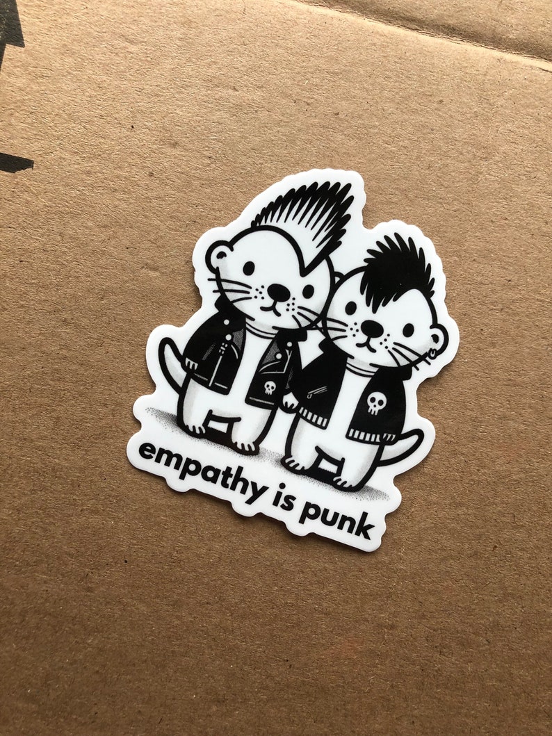 Peut inclure: Autocollant noir et blanc repr&eacute;sentant deux loutres de dessin anim&eacute; portant des vestes en cuir et des cr&ecirc;tes iroquoises. Les loutres sont debout c&ocirc;te &agrave; c&ocirc;te et le texte "empathy is punk" est imprim&eacute; en dessous.