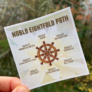 May include: A square sticker with the words "NOBLE EIGHTFOLD PATH" in brown text. The sticker features a gold-colored wheel design and lists eight principles: Right View, Intention, Speech, Action, Livelihood, Effort, Concentration, and Mindfulness.