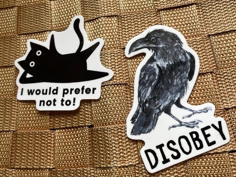 May include: Two stickers on a textured surface. One features a black cat with the text "I would prefer not to!". The other is a detailed illustration of a raven with the word "DISOBEY".