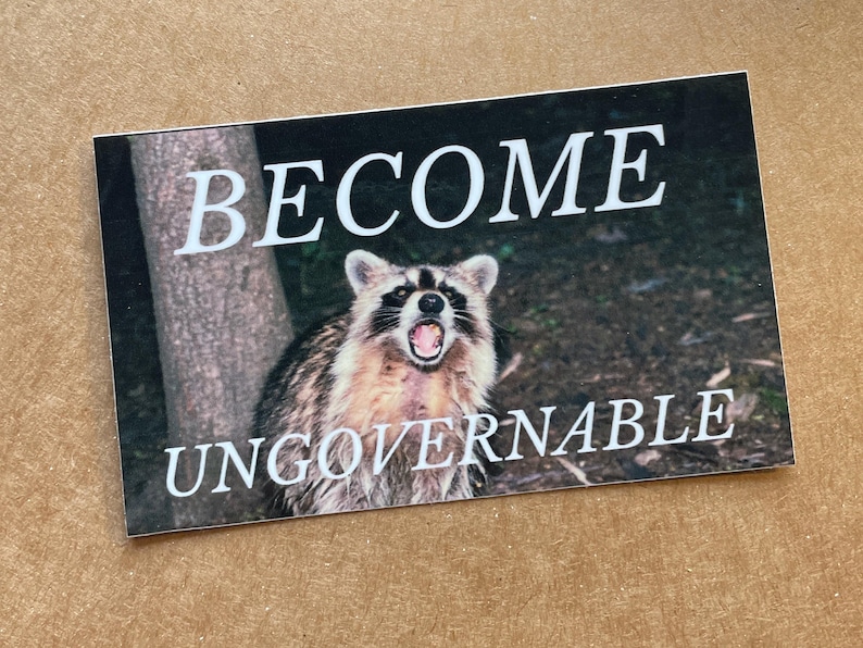 Op de afbeelding: Een sticker met een wasbeer met zijn bek open en de tekst "BECOME UNGOVERNABLE" in witte letters.