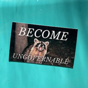 Op de afbeelding: Een sticker met een wasbeer met zijn bek open en de tekst "BECOME UNGOVERNABLE" in witte letters.