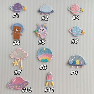 May include: Eleven embroidered iron-on patches featuring various space-themed designs, including planets, rockets, clouds, and astronauts. The patches are numbered 1 through 11.