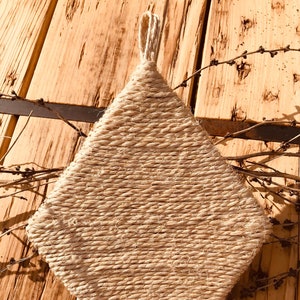 Puede incluir: Un posavasos de forma de diamante beige hecho de cuerda trenzada. El posavasos está sobre una superficie de madera.