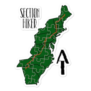 May include: A sticker featuring a green map of the eastern United States, composed of puzzle pieces, with a red trail line. The words "SECTION HIKER" are above the map, and a black arrow pointing up is to the right.