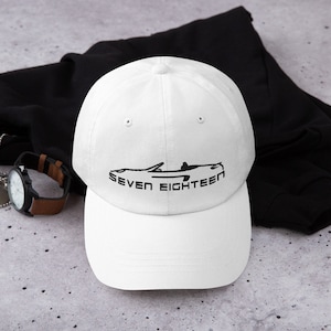 Op de afbeelding: Witte baseballpet met een zwart silhouet van een cabriolet en de tekst "SEVEN EIGHTEEN" geborduurd op de voorkant.