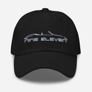 Könnte beinhalten: Schwarze Baseballkappe mit gebogenem Schirm. Auf der Kappe steht der Text "NINE ELEVEN" in einer stilisierten Schriftart, zusammen mit einer Auto-Umrisszeichnung in einer helleren Farbe. Der Hut ist ein klassischer, verstellbarer Stil.