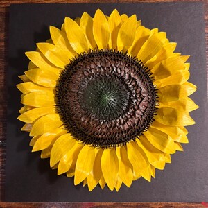 Peut inclure: Une &oelig;uvre d'art repr&eacute;sentant un tournesol avec des p&eacute;tales jaune vif et un centre brun fonc&eacute;. Le tournesol est pos&eacute; sur un fond sombre, mettant en valeur ses couleurs vives et ses d&eacute;tails complexes. Une pi&egrave;ce d'art floral.