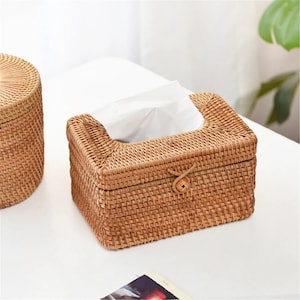 May include: A woven wicker tissue box cover with a brown color and a woven lid with a leather tie closure.
