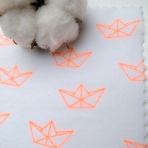 Peut inclure: Tissu blanc avec un motif répété de bateaux en papier origami orange. Le tissu est texturé et a un aspect légèrement froissé.