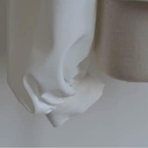 May include: Close-up of a white fabric sleeve with a gathered detail at the cuff.