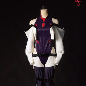 May include: A purple and white cosplay costume with a black belt and red accents. The costume is on a mannequin against a black background. Kiki x Costume.