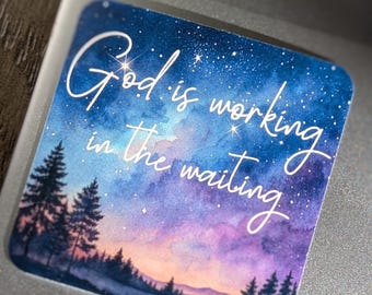 May include: A square sticker with a watercolour design of a starry night sky in shades of blue, purple, and pink. The sticker features the text "God is working in the waiting" in elegant white script, with a silhouette of pine trees at the bottom.
