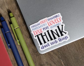 May include: A sticker with the words "THINK about such things" and other positive words in a colourful design. Two pens, one blue and one green, and a red notebook are also visible on a wooden surface next to a laptop.