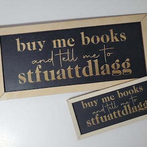 May include: Two wooden signs with black backgrounds and gold lettering. The signs read "buy me books and tell me to stfuattdlagg".