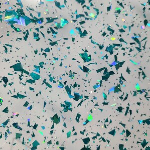 Puede incluir: Un fondo blanco con purpurina iridiscente azul verdosa esparcida.