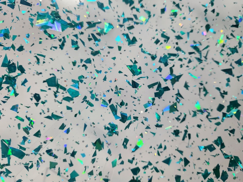Puede incluir: Un fondo blanco con purpurina iridiscente azul verdosa esparcida.