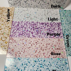 Puede incluir: Primer plano de siete papeles de purpurina de diferentes colores. Los colores son amarillo, blanco, morado, rosa, azul, verde claro y verde oscuro.