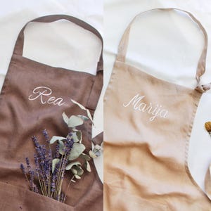 May include: Two brown linen aprons with white embroidered names, "Rea" and "Marija".