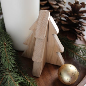 May include: A wooden Christmas tree ornament with a gold ornament on a wooden tray with pine branches and a white candle.