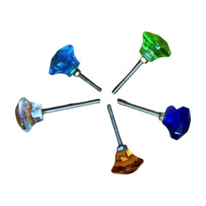 May include: Six colorful glass cabinet knobs arranged in a circular pattern. The knobs are faceted and come in shades of blue, green, clear, and amber. Each knob has a silver-colored threaded post for attachment.