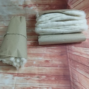 Puede incluir: Dos rollos de bolas de algod&oacute;n blancas envueltos en papel marr&oacute;n. Las bolas de algod&oacute;n est&aacute;n apiladas y listas para usar.