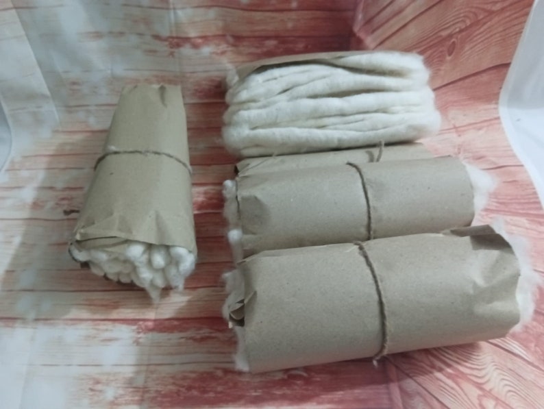 Puede incluir: Cuatro rollos de bolas de algod&oacute;n blancas envueltos en papel marr&oacute;n. Las bolas de algod&oacute;n est&aacute;n bien apretadas y el papel est&aacute; atado con una cuerda.